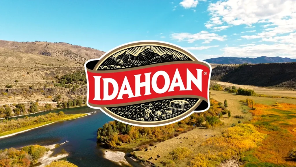 A landscape of a winding river through grassy, rolling hills under a partly cloudy sky, with the Idahoan Potatoes logo prominently displayed in the center, reflecting our commitment to quality enjoyed by families everywhere.