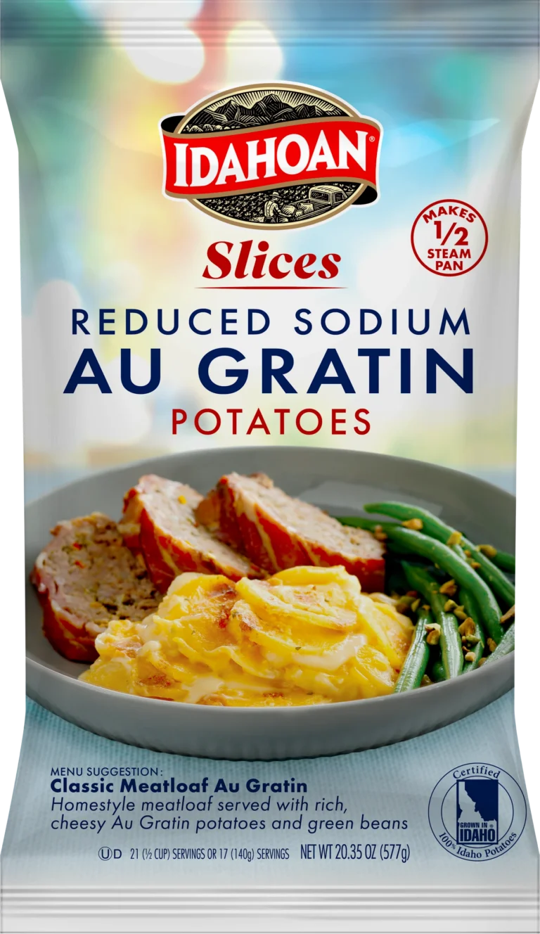 A package of Idahoan Reduced Sodium Au Gratin Potatoes, featuring sliced potatoes covered in a cheesy sauce, served alongside meatloaf and green beans on a plate. The packaging highlights that it serves half a steam pan and is Idaho certified.